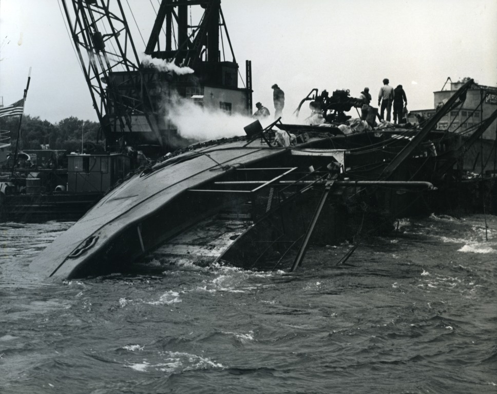 Workers use an old steam-powered pump to suction oil through the side of the capsized SIDNEY E. SMITH, JR.