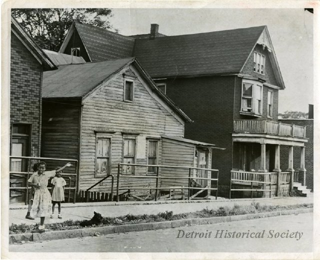 The wooden house on the left stood at 1822 Macomb Street and was occupied by the young Ralph Bunche and his extended family during part of his childhood. The house is pictured here in the early 1950s. The house no longer stands, and the plot on which it stood on is now part of the Dequindre Cut.