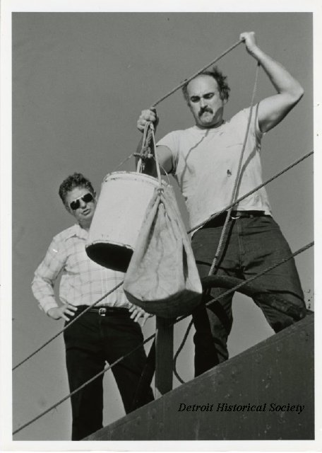 A sailor pulling up the mail in a pail from the J.W. WESTCOTT II, 1975 - 2012.022.542